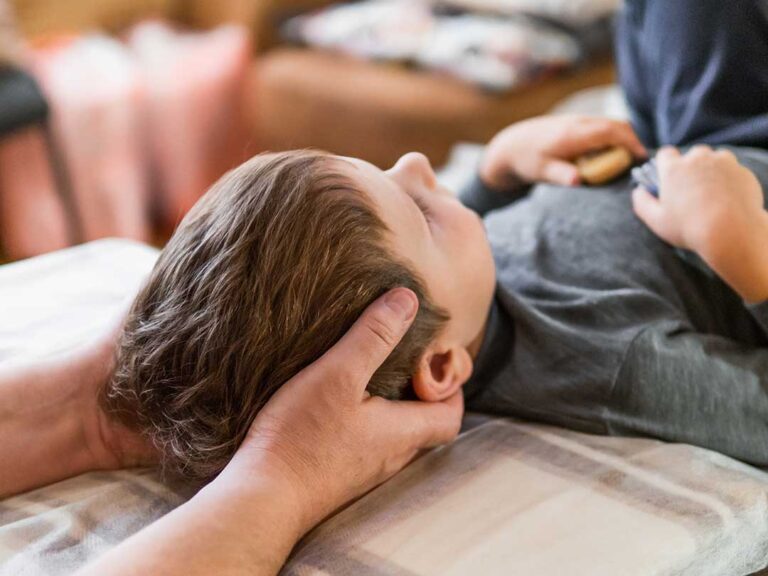 Person resting in bed while gently stretching a stiff neck beside a supportive pillow